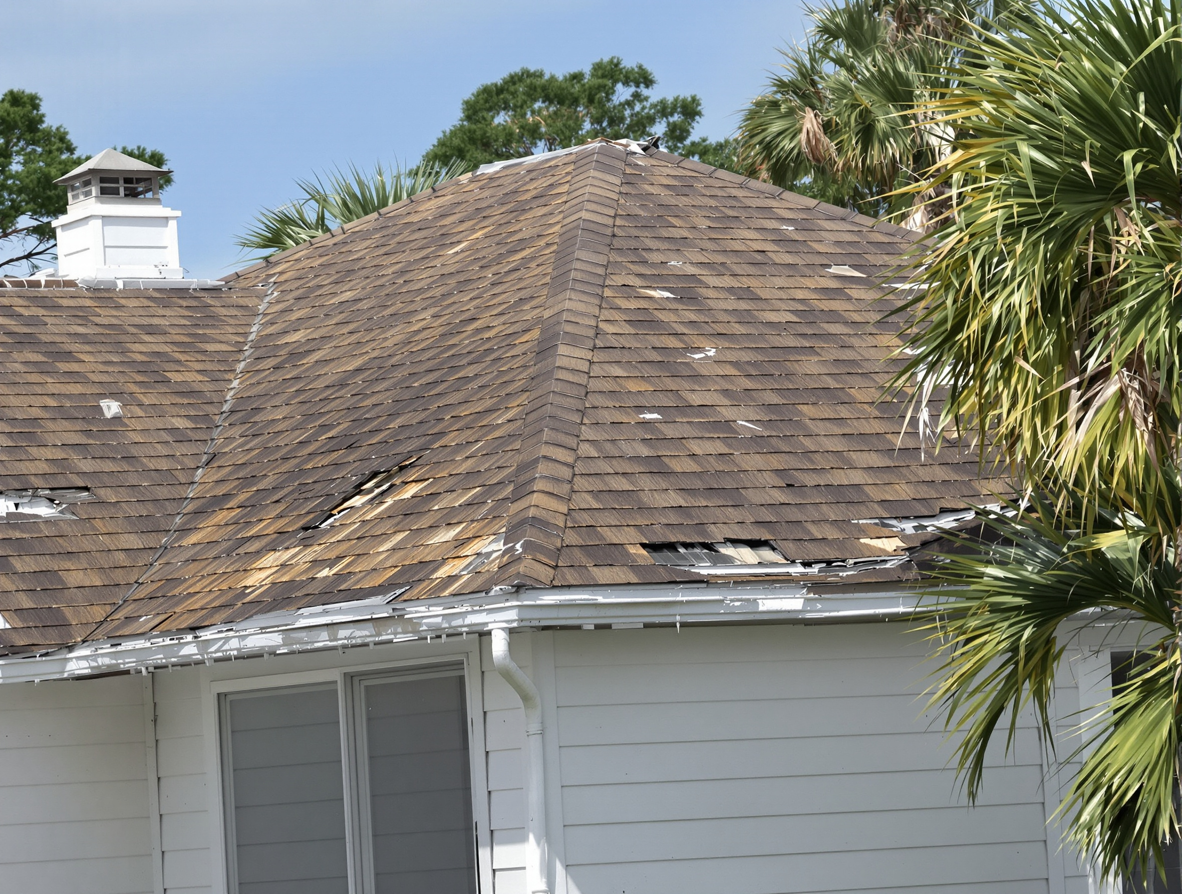 Two-story coastal home in Gulf Shores Alabama with wind-damaged brown asphalt shingles and lifted tabs — before metal roof replacement
