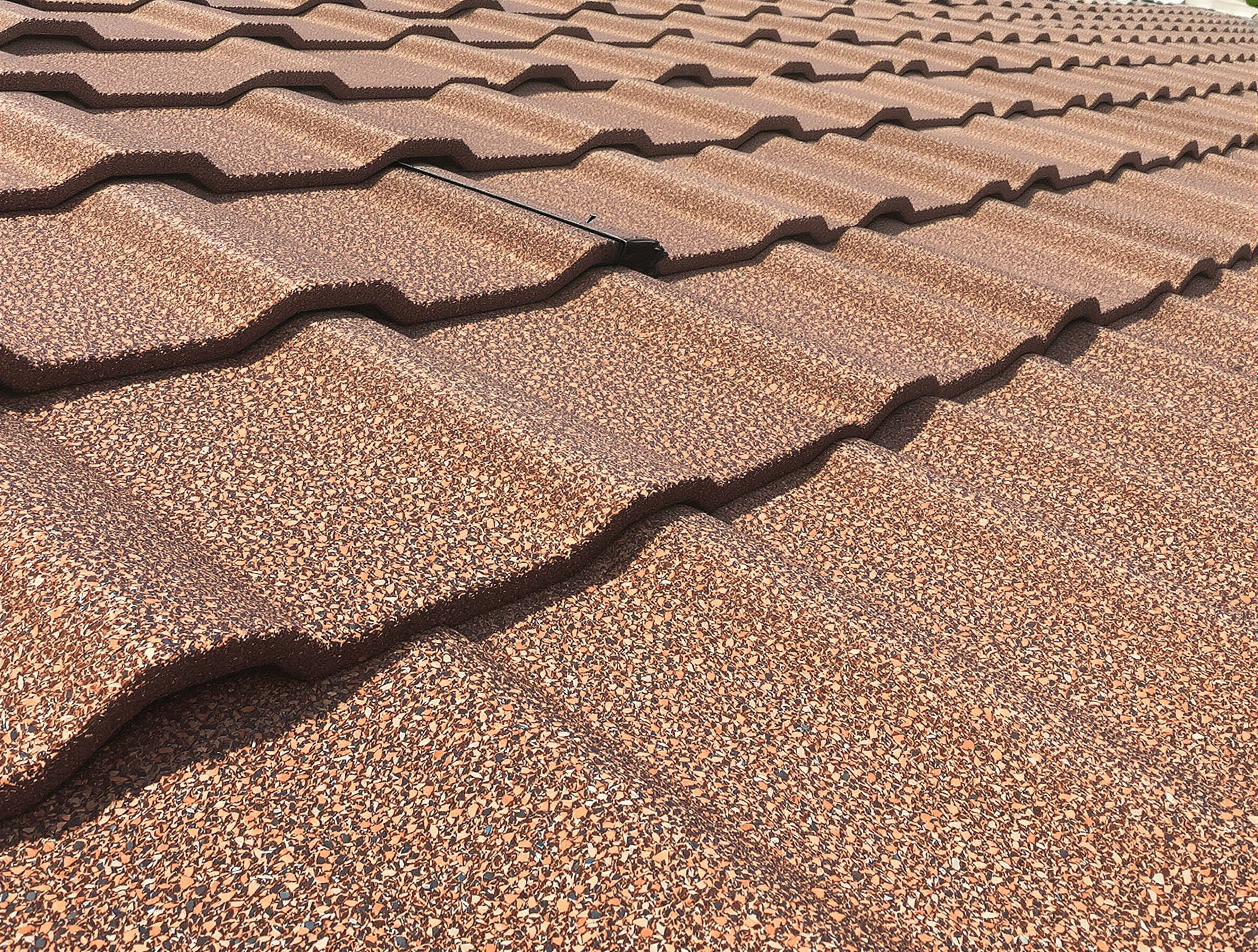 Close-up of stone-coated steel roofing showing ceramic granule texture and interlocking tile profile, earth tone brown